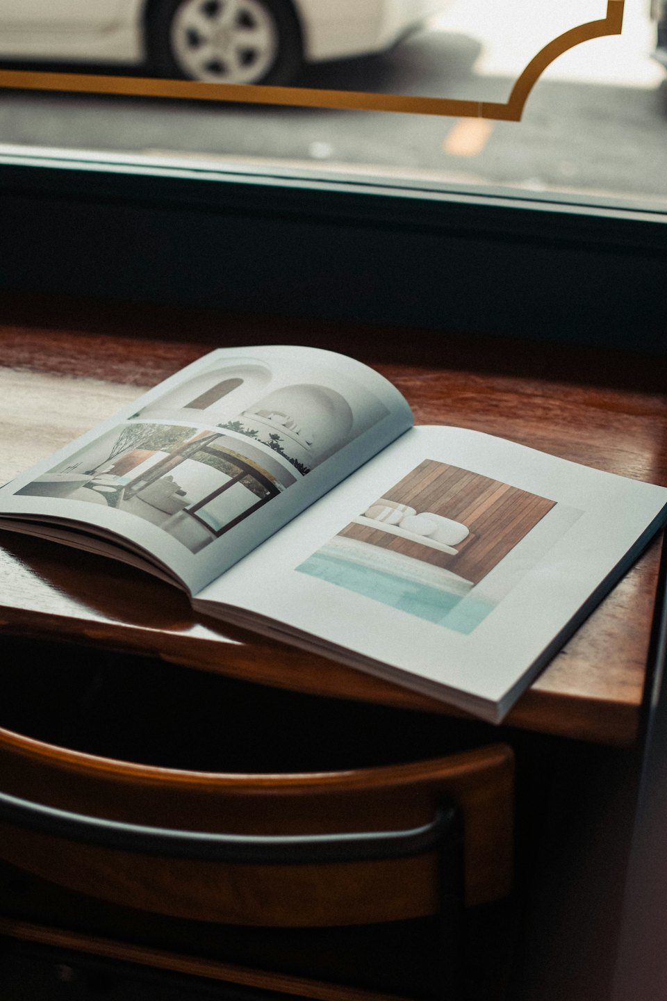 Open design magazine resting on a wooden table near windows.