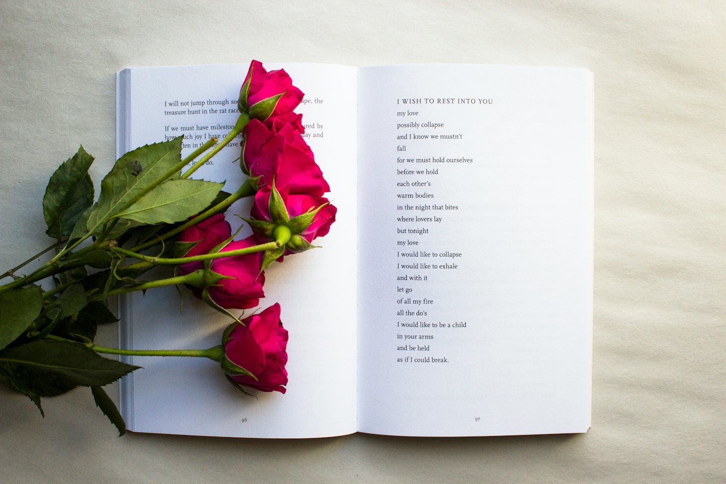 Open book with poetry next to pink rosebuds.