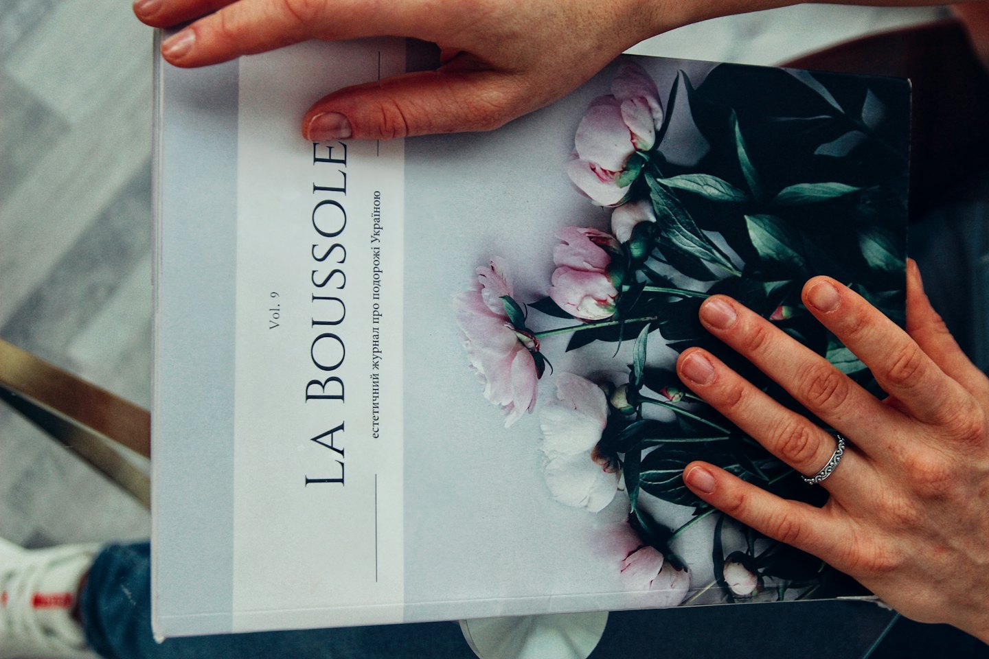 Hands hold an open magazine featuring pink peonies.