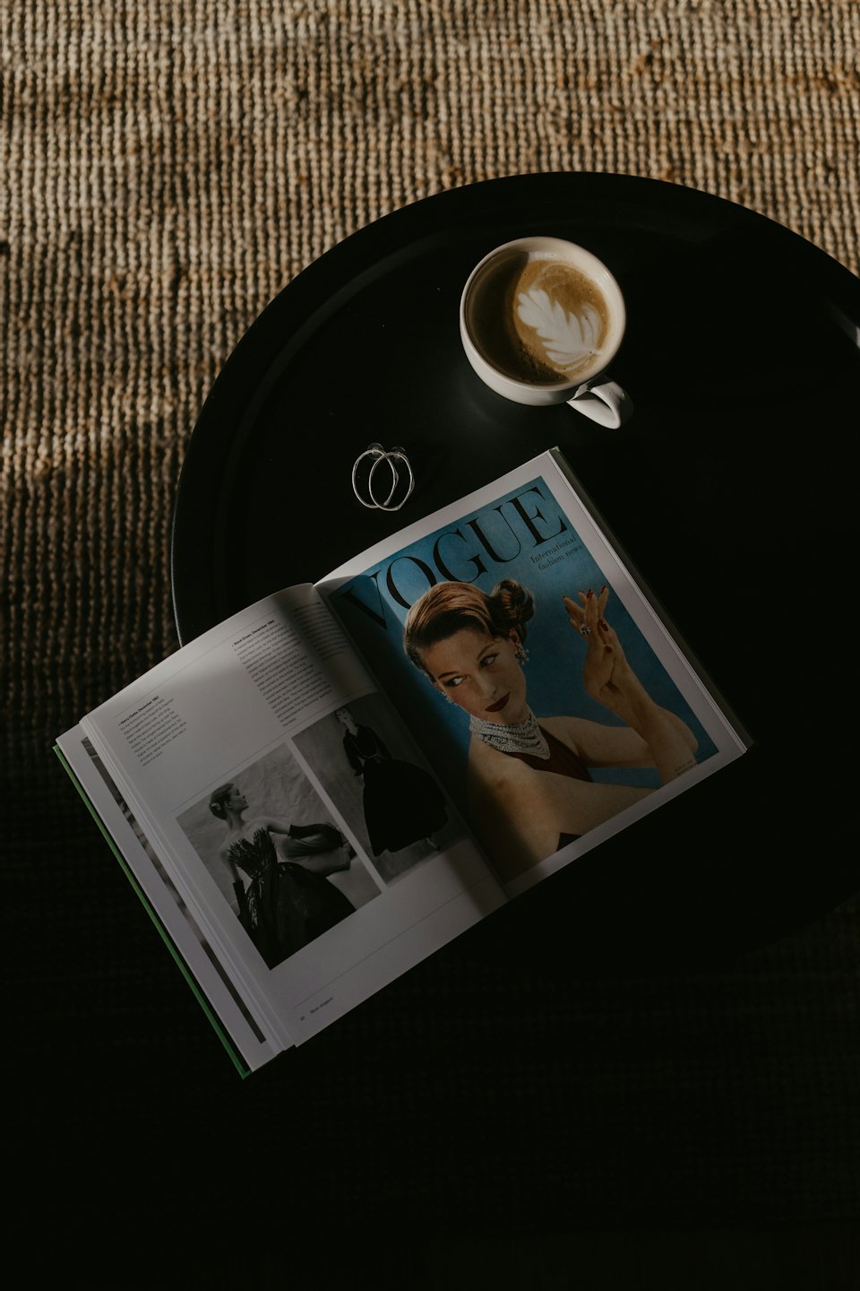 Open fashion magazine with coffee and earrings on a table.